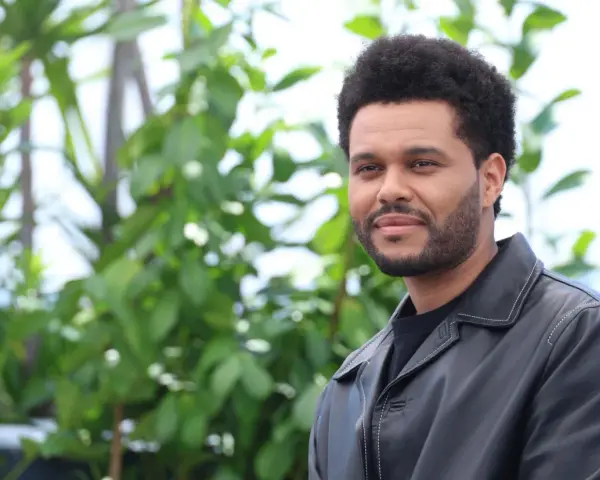 The Weeknd trägt eine schwarze Lederjacke vor einem grünen, unscharfen Hintergrund.