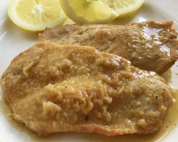 Deliziose scaloppine al limone, succulente e dorate, servite con spicchi di limone fresco.