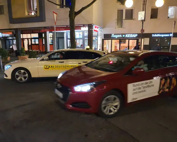 Ein weißes Taxi und ein rotes Auto mit Uber-Werbung stehen nebeneinander. Der Unterschied über Taxi ist die moderne Alternative.