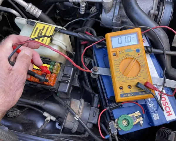 Testing for a parasitic draw with a multimeter connected to the car battery. A reading of 01.0 mV indicates a small current drain.
