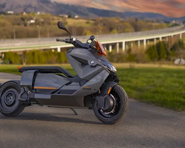 Szary skuter elektryczny BMW CE 04 na tle malowniczego krajobrazu z mostem i wzgórzami.