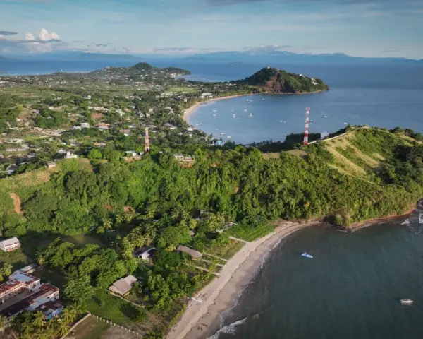 Malownicze miasto na Madagaskarze z zielonymi wzgórzami, plażą i zatoką pełną łodzi. W oddali góry.