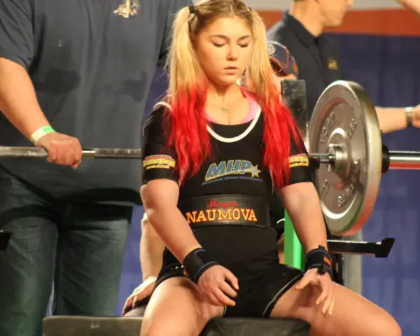 Młoda sportsmenka z rudymi pasemkami włosów przygotowuje się do wyciskania na klatę. Czy to będzie nowy rekord świata?
