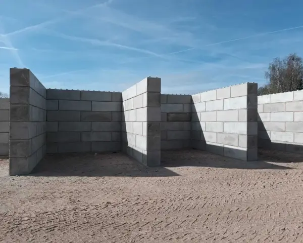 Budowa muru oporowego z betonowych bloczków na piaszczystym podłożu.