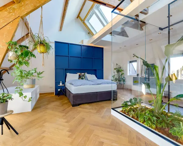 Mansarde da sogno con letto blu, piante sospese e un giardino interno in vetro. Travi a vista e lucernari creano un'atmosfera unica.