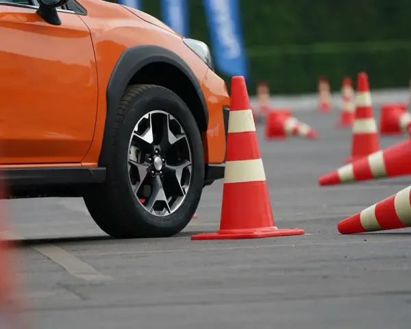 Pomarańczowy samochód na placu manewrowym, otoczony pachołkami. Zastanawiasz się, ile kosztuje prawo jazdy?