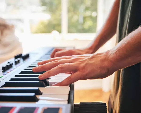Dłonie grające na keyboardzie. To instrument muzyczny, który pozwala tworzyć melodie.