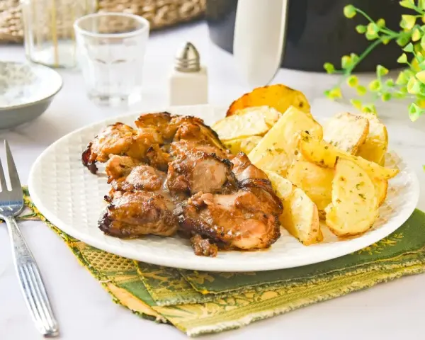Contramuslos de pollo jugosos y dorados con patatas asadas en un plato blanco.