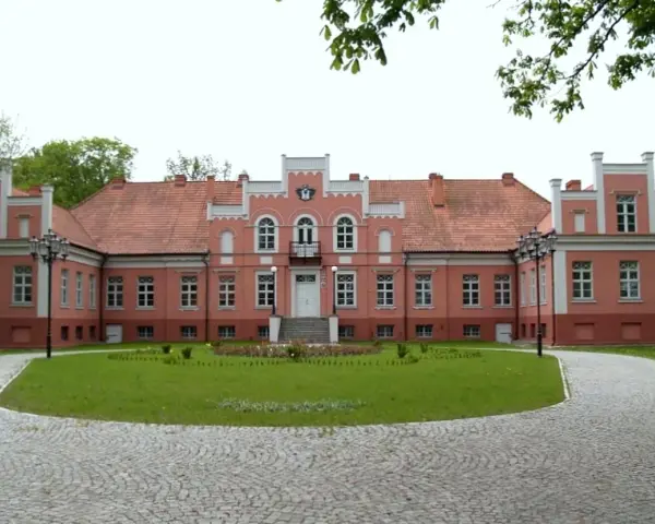 Pałac Przebendowskich w Wejherowie, różowy, z czerwonym dachem, otoczony zielenią i brukowanymi alejkami.