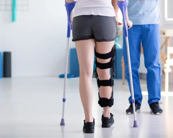 Rehabilitacja stopy po złamaniu: pacjentka z ortezą i kulami ćwiczy pod okiem fizjoterapeuty.