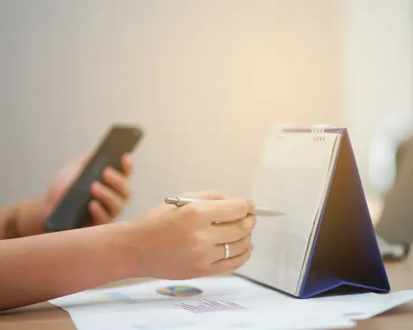 Ręce planują zadania na kalendarzu, trzymając telefon. Zapewnia to ciągłość pracy i organizację dnia.