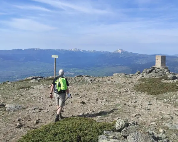 Senderista camina hacia el **puerto de Navafría**, con un mojón y montañas nevadas al fondo.