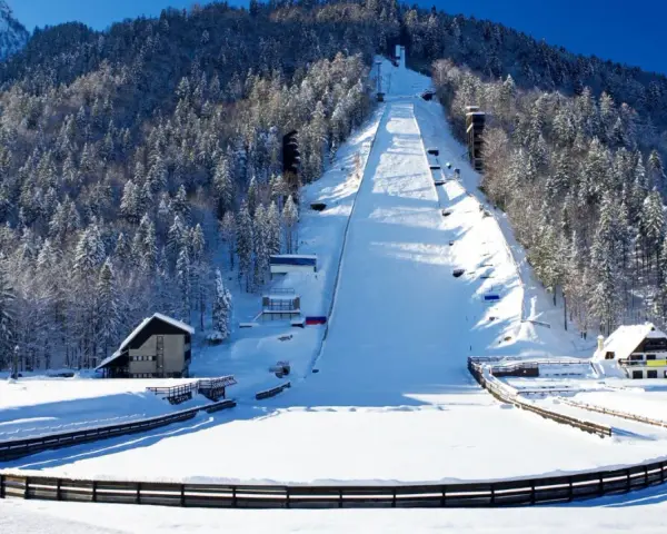 Zimowa Planica w Alpach Julijskich, z ośnieżoną skocznią narciarską i lasem iglastym.
