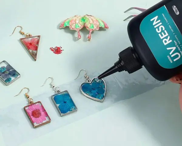 A hand applies UV resin to a heart-shaped earring with blue flowers, demonstrating how UV resin works to create beautiful jewelry.