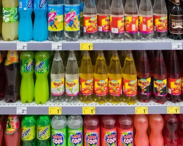Półki sklepowe z różnymi napojami gazowanymi w plastikowych butelkach.