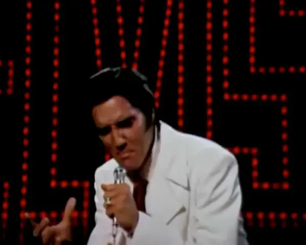 Elvis Presley singt "If I Can Dream" in einem weißen Anzug vor einer roten Lichterwand.