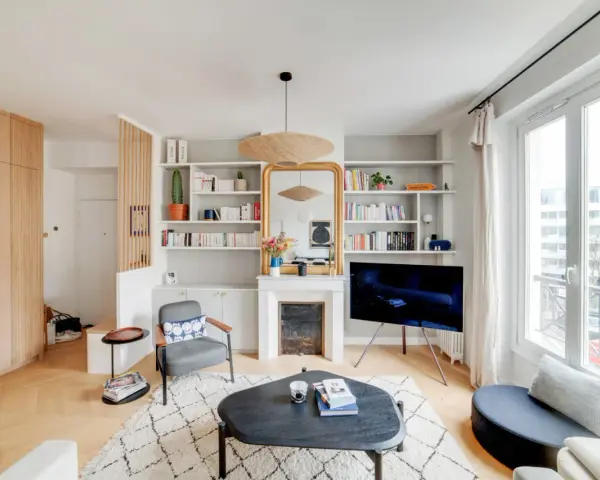 Aménagement entrée ouverte avec rangements boisés, fauteuil, cheminée décorative et étagères remplies de livres.