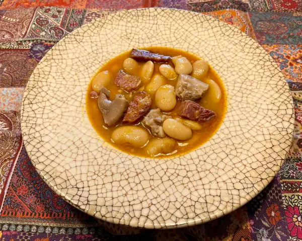 Plato de judiones de la granja receta tradicional, con trozos de tocino y carne en un caldo sabroso.