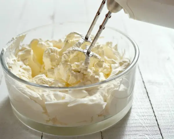 Ubita śmietanka kremówka w szklanej misce, przygotowywana mikserem. Idealna do deserów.