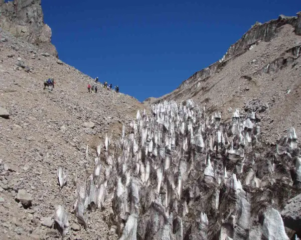 Grupa turystów wspina się po kamienistym zboczu w kierunku lodowych formacji, przypominających zęby. To krajobraz, który może prowadzić na najwyższy szczyt Andów.