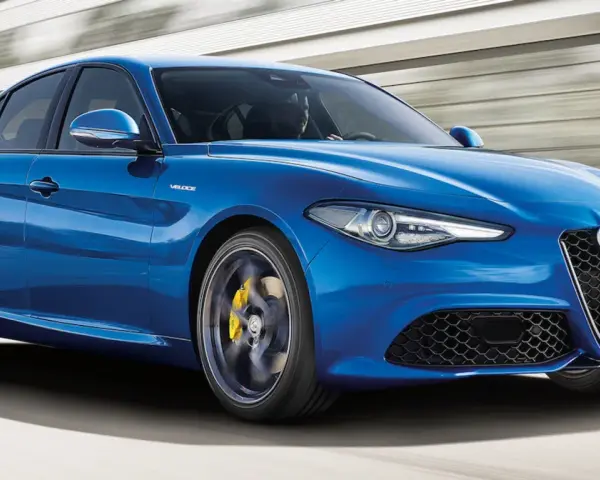 Błękitne Alfa Romeo Giulia Veloce pędzi po drodze, ukazując sportowy charakter i dynamiczną sylwetkę.
