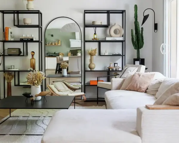 Soggiorno con divano bianco, librerie nere, specchio ad arco e cactus. Un'oasi di pace in stile casa minimal.