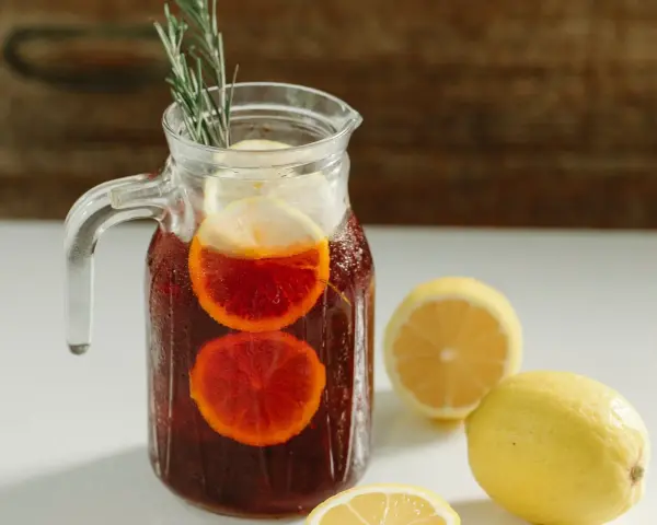 Dzbanek orzeźwiającej sangrii wino z plasterkami pomarańczy i cytryny, ozdobiony gałązką rozmarynu.