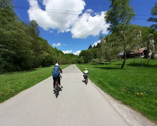Dwie osoby na rowerach przemierzają malownicze **ojcowskie park narodowy trasy rowerowe**. Słoneczny dzień, zieleń i chmury na niebie.