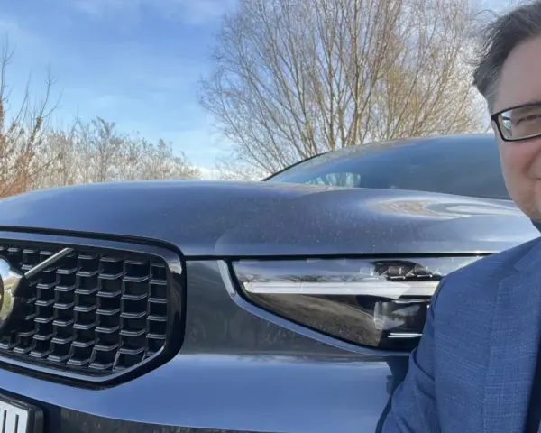 Mężczyzna w okularach i garniturze pozuje do zdjęcia z przodu Volvo XC40. Czy są jakieś wady tego modelu?