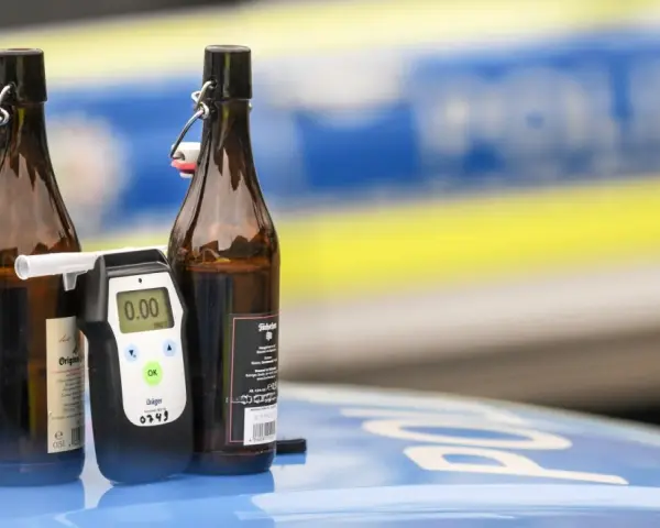 Zwei Bierflaschen und ein Alkoholtester auf einem Polizeiauto. Der Tester zeigt 0.00, aber die Gefahr einer 1 1 Promille Strafe bleibt.