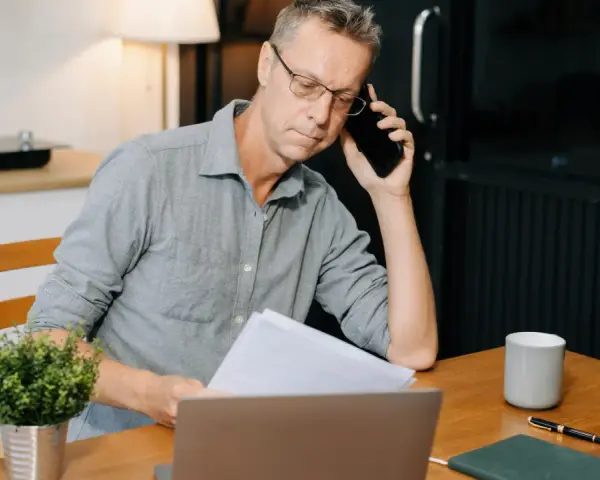 Mann am Telefon, der Dokumente prüft. Frustriert, weil die Kfz-Versicherung nicht zahlt.