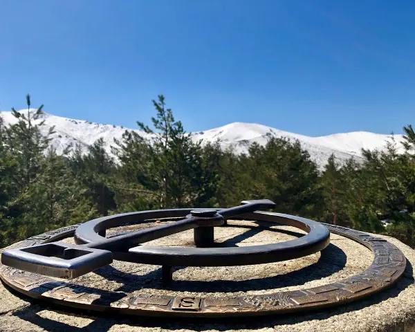 Un mirador de la gitana con un compás de bronce y montañas nevadas al fondo.