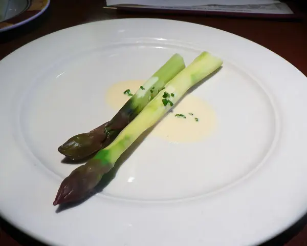 Zwei Spargelstangen auf einem Teller, serviert mit einer cremigen beurre blanc Sauce und gehackten Kräutern.