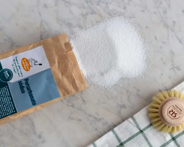 Percarbonato sódico, ideal para ropa color, se derrama de su bolsa junto a un cepillo.