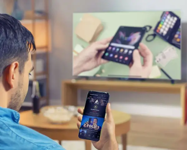 Mann verbindet sein Handy mit dem Fernseher, um ein Video anzusehen. Auf dem Handy ist ein YouTube-Video zu sehen.