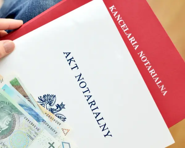 Dłoń trzyma dokument "Akt Notarialny" z Kancelarii Notarialnej, obok leżą polskie banknoty.