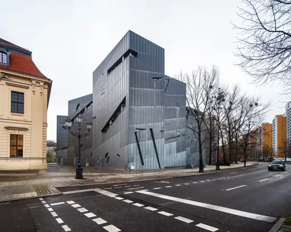 Nowoczesny budynek Muzeum Żydowskiego w Berlinie, obok zabytkowej kamienicy, z charakterystyczną, poszarpaną fasadą.