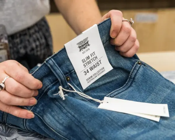 Dłonie trzymają niebieskie jeansy z metką "SLIM FIT STRETCH 34 WAIST". Idealny rozmiar jeansów dla Ciebie.