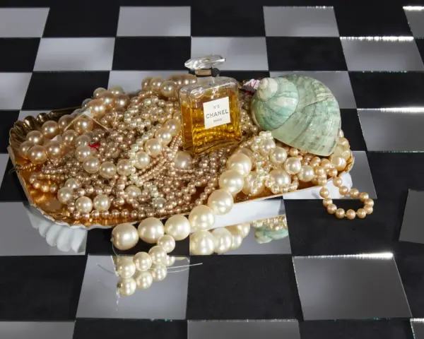 Perle, profumo Chanel N°5 e una conchiglia su un vassoio dorato. Il profumo evoca il **chanel significato** di lusso e raffinatezza.