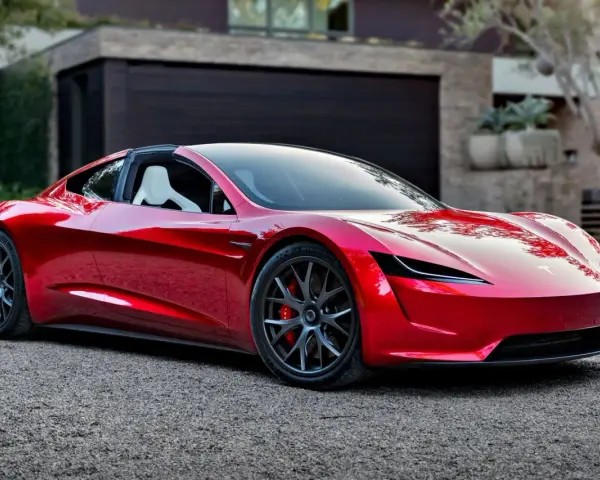 Błyszczący, czerwony Tesla Roadster 2 z białymi siedzeniami stoi przed nowoczesnym domem.