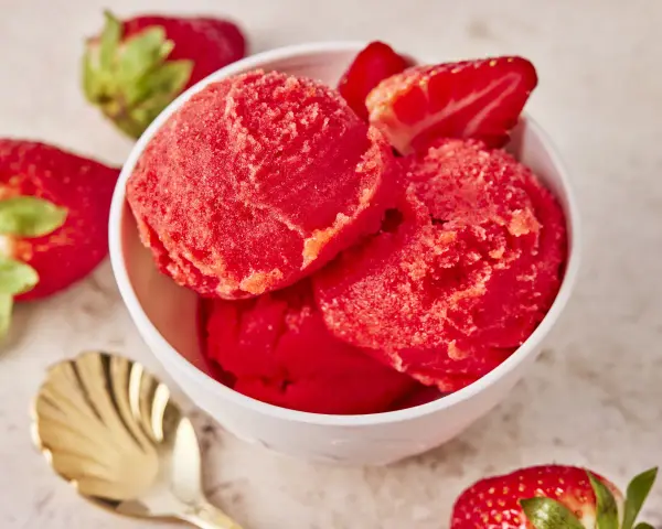Schüssel mit erfrischendem Erdbeer Sorbet, garniert mit frischen Erdbeeren und einer goldenen Löffel.