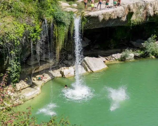 Disfrutando del baño en piscinas naturales junto a la cascada de Tobera. Un grupo de amigos se lanza al agua turquesa.