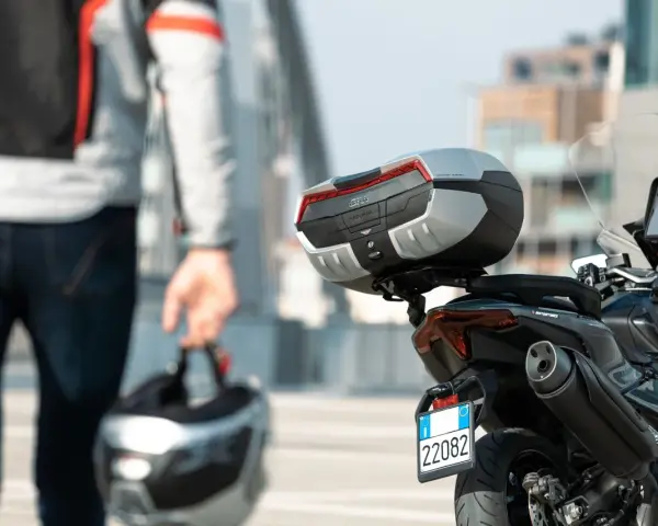 Un motociclista con casco in mano si avvicina alla sua moto. Andare in moto fa bene, un'avventura ti aspetta!