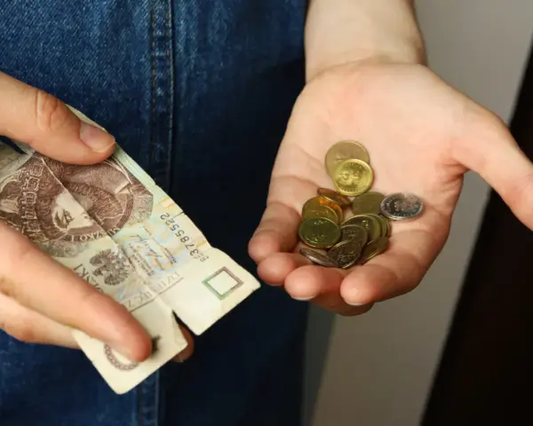 Dłoń trzyma banknot 20 zł i garść monet. Symbolizuje to spłatę długu po wyroku sądowym, gdzie każda złotówka ma znaczenie.