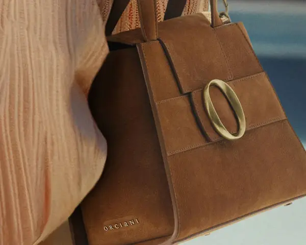 Borsa in camoscio marrone con fibbia dorata. La texture morbida evidenzia la differenza tra camoscio e pelle scamosciata.