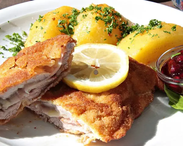 Kotlet po szwajcarsku z ziemniakami, cytryną i żurawiną. Pyszne danie na talerzu.