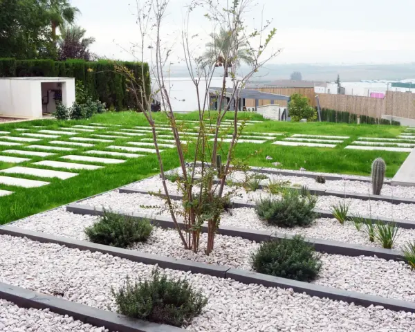 Vialetti giardino moderni con lastre quadrate su prato verde e aiuole di ghiaia bianca con piante succulente e arbusti.