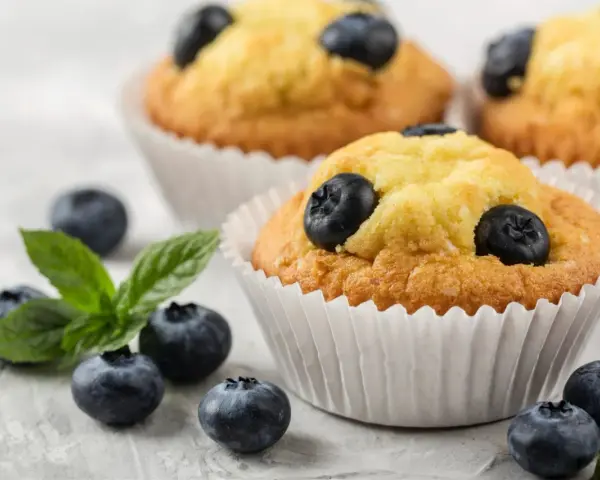 Pyszne muffiny z borówkami, ozdobione świeżymi owocami i listkiem mięty. Idealne na deser.