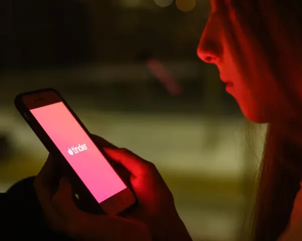 Dziewczyna patrzy na ekran telefonu z logo Tindera. Zastanawia się, co odpisać na "czego szukasz na Tinderze?".