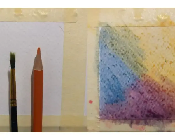 Un pinceau et un crayon aquarelle orange sont prêts pour l'utilisation. Une zone de papier présente des dégradés de couleurs vives.